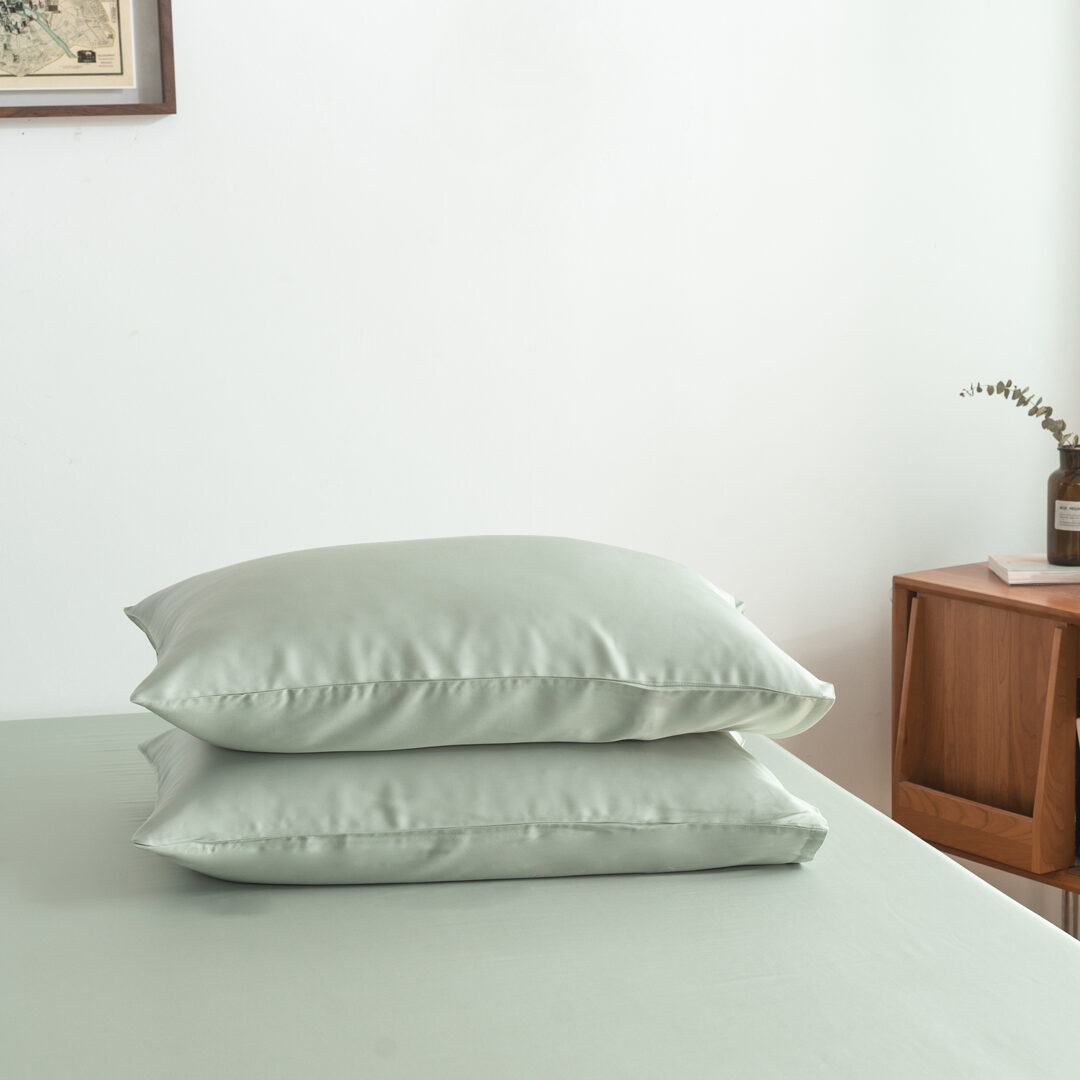 Foto van vooraanzicht van twee kussenslopen Sage Green op een bed (kleur licht groen)