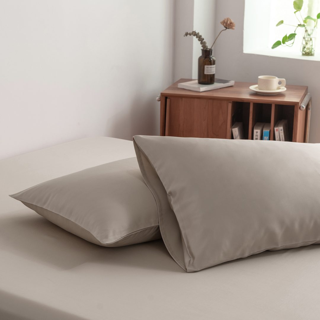 Foto van zijaanzicht van twee kussenslopen Soft Taupe op een bed (kleur licht bruin)