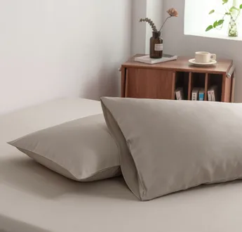 Foto van zijaanzicht van twee kussenslopen Soft Taupe op een bed (kleur licht bruin)