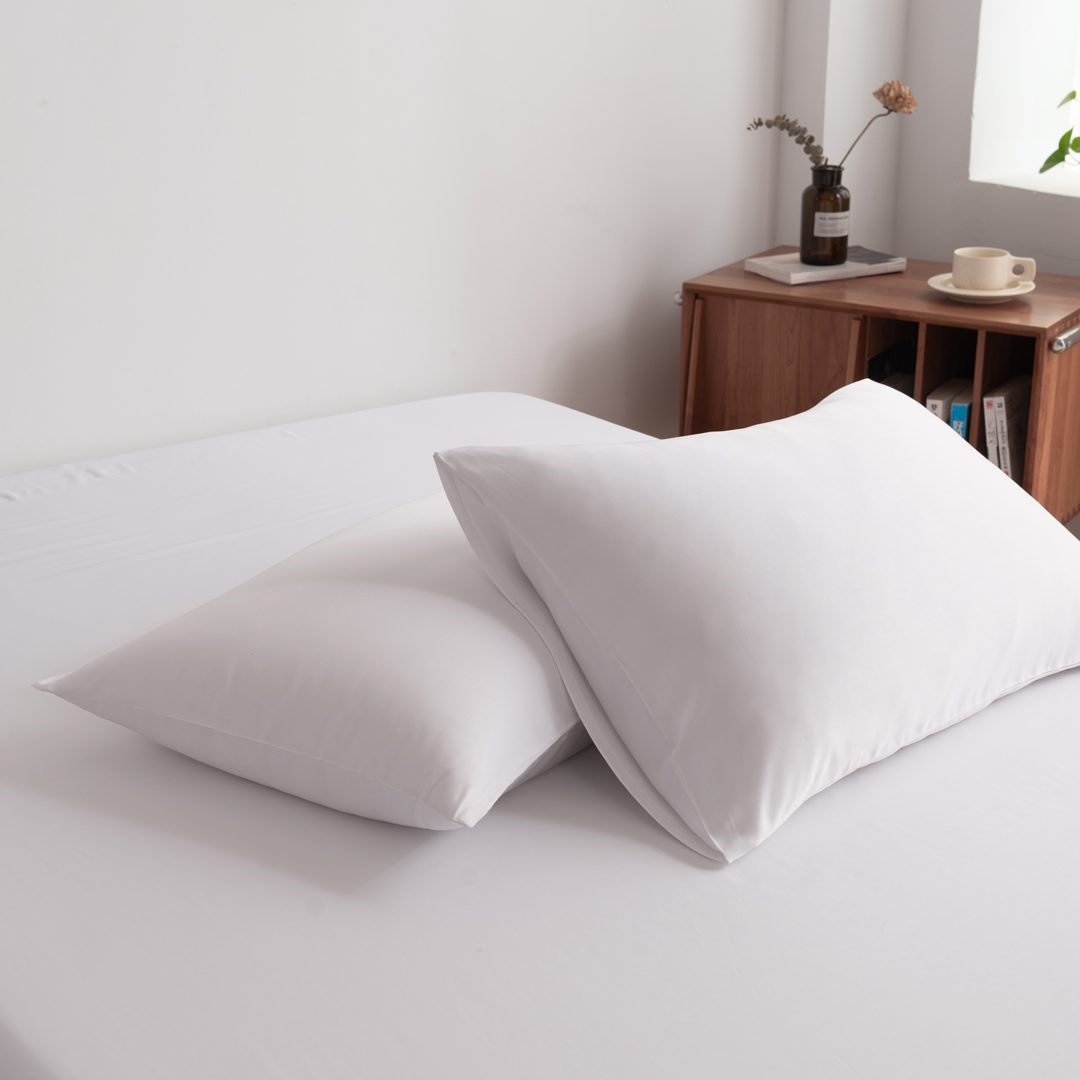 Foto van zijaanzicht van twee kussenslopen Coco White op een bed (kleur wit)