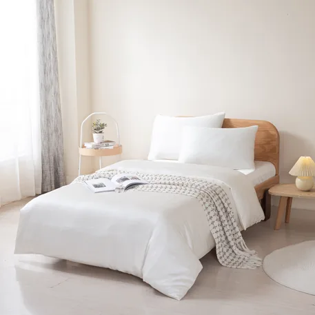 Bamboo duvet cover and pillowcases in cream on a made bed in a bright bedroom, angled view