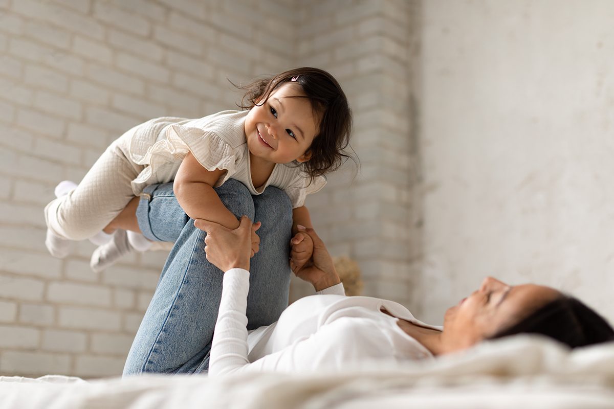 Een vrouw maar haar kind in de lucht op een bed met bamboe beddengoed