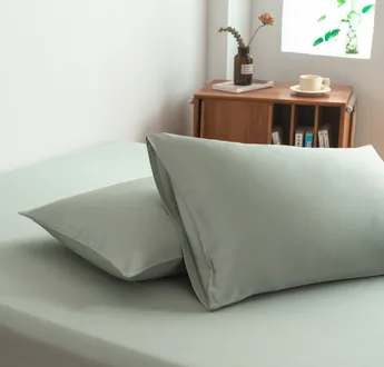 Twee bamboe kussenslopen Sage Green (saliegroen) naast elkaar op een bed