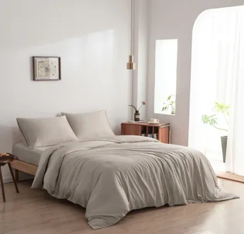Bamboe dekbedovertrek en kussenslopen Soft Taupe (taupe) op een opgemaakt bed in een lichte slaapkamer, schuin aanzicht
