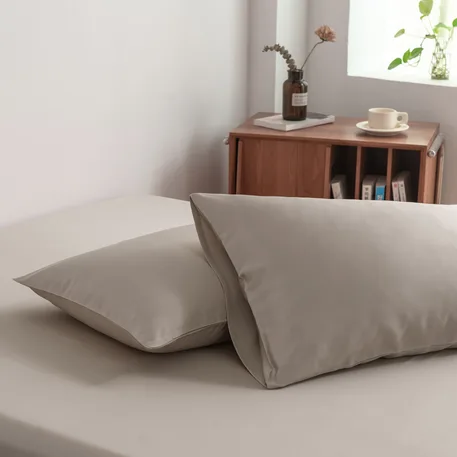 Foto van zijaanzicht van twee kussenslopen Soft Taupe op een bed (kleur licht bruin)