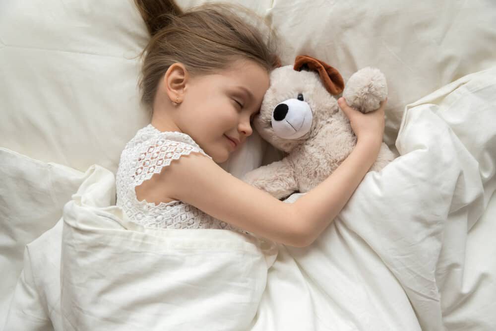 Foto van een kindje die ligt te slapen met haar knuffeltjes in bamboe beddengoed