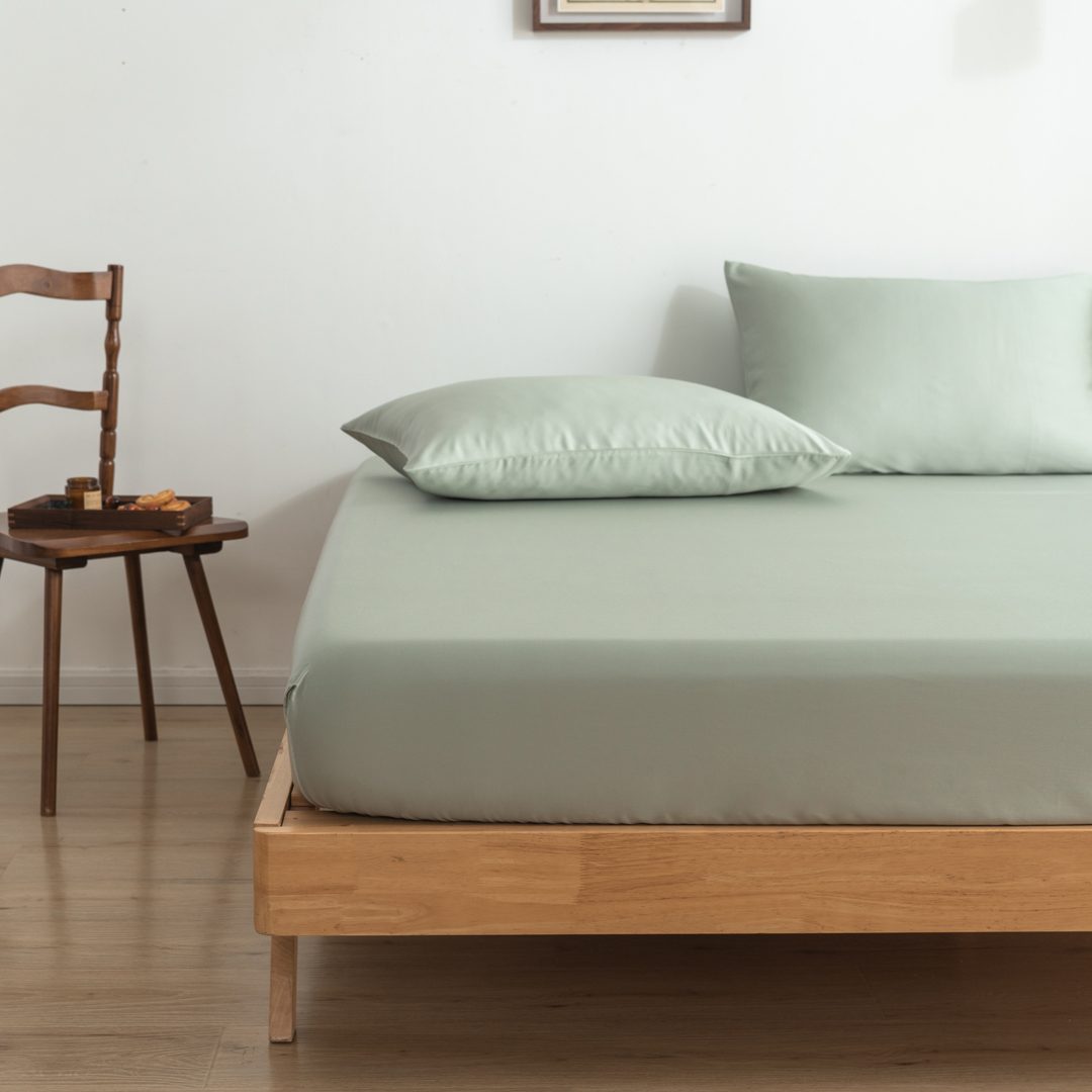 Twee kussenslopen Sage Green op een bed als sfeerfoto (kleur licht groen)